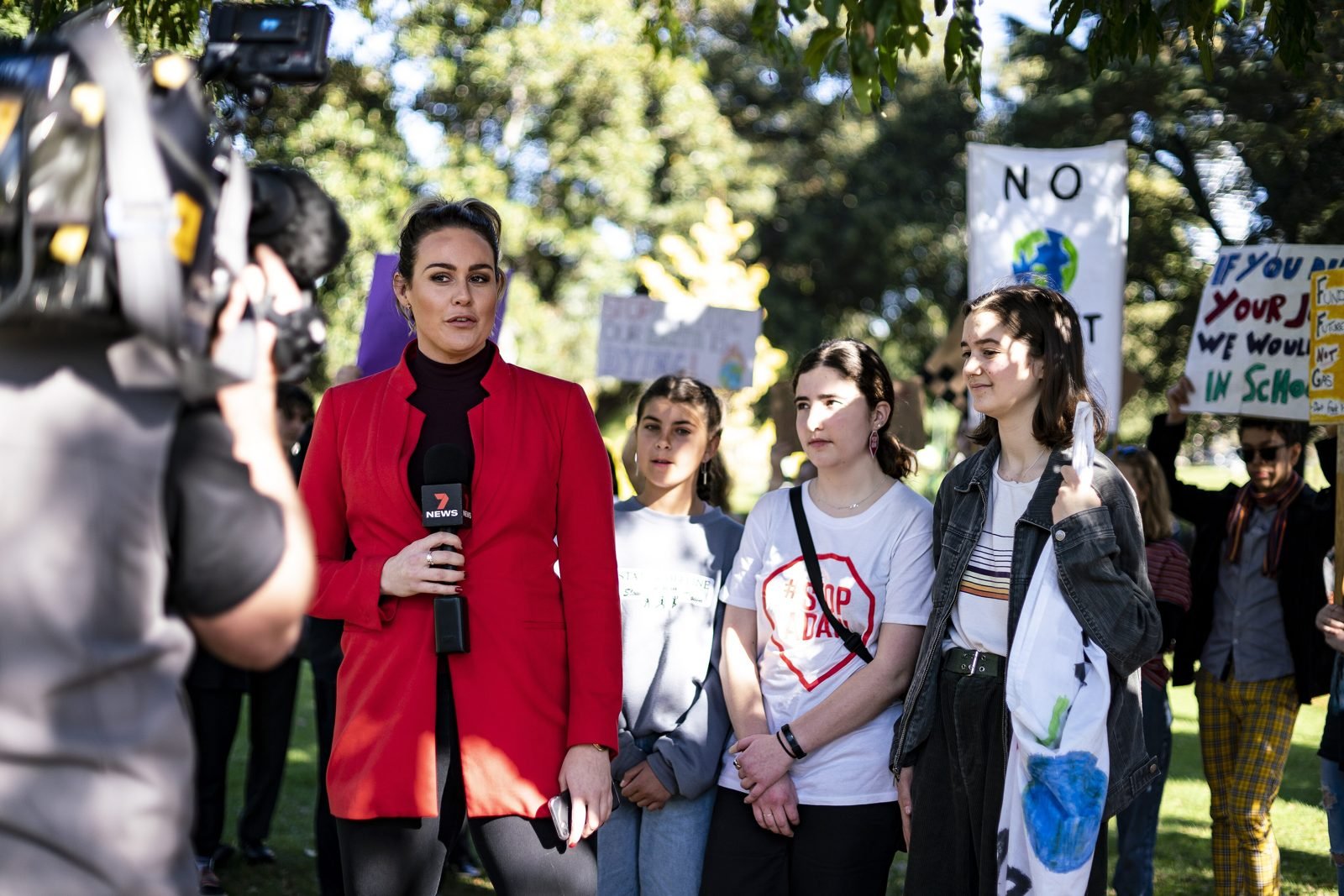 A television journalist reports live from a school climate strike in Melbourne as a camera operator films