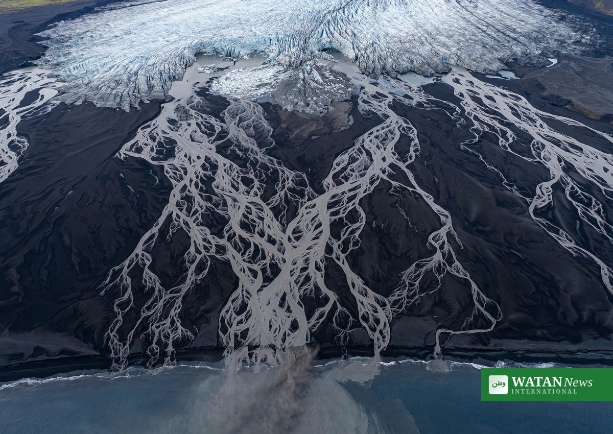 Aerial view of a retreating Icelandic glacier with braided meltwater rivers flowing over black volcanic sand toward the ocean