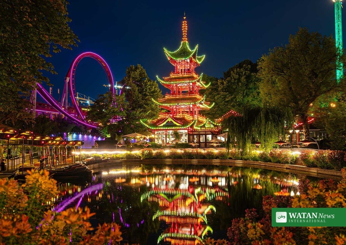 Tivoli om aftenen med den oplyste japanske pagode og forlystelsernes lys spejlet i Tivoli Sø