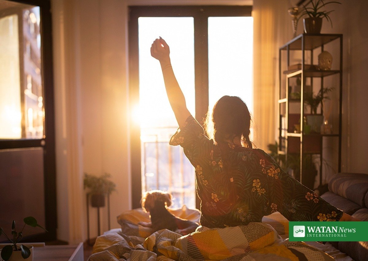Woman wakes up and stretches in morning sunlight, healthy sleep wellness