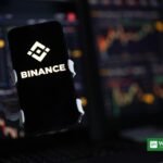 Binance logo on a smartphone against cryptocurrency trading charts