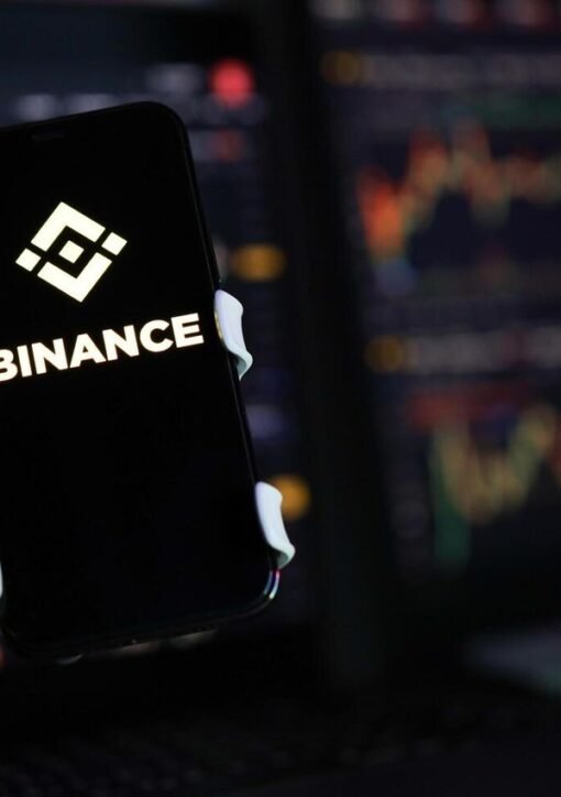 Binance logo on a smartphone against cryptocurrency trading charts