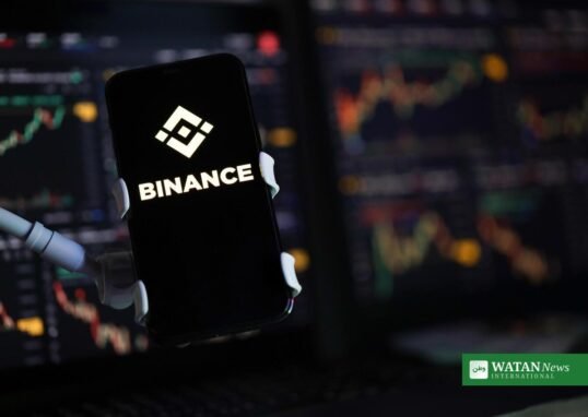 Binance logo on a smartphone against cryptocurrency trading charts