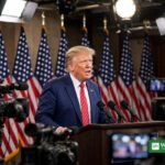 Donald Trump at a podium with American flags and TV cameras amid the taxpayer-funded ads controversy