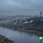 Kyiv skyline at dawn with the Motherland Monument and golden-domed churches, glow of distant explosions on the horizon after Russian strikes on Kyiv energy facilities