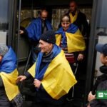 Oleshky evacuees draped in Ukrainian flags disembarking a bus on arrival in Ukraine