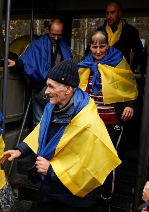 Oleshky evacuees draped in Ukrainian flags disembarking a bus on arrival in Ukraine