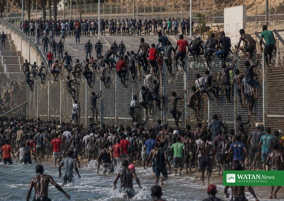 Migrants climb the Ceuta border fence as Spanish police stand guard