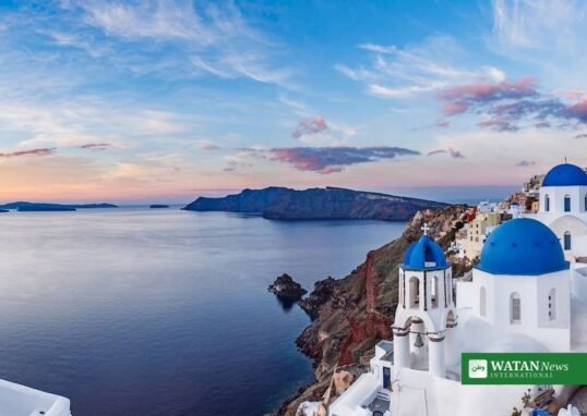 Wide panoramic view of Santorini caldera at sunset with blue-domed churches